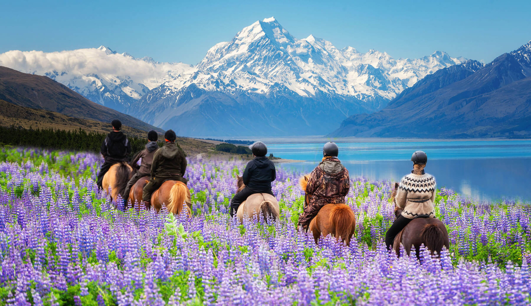 Group traveling riding horses around a lake with a mountain in the background