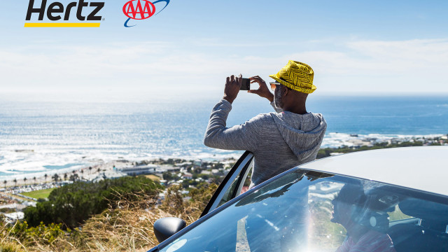 A man taking photo of the ocean with his car behind him