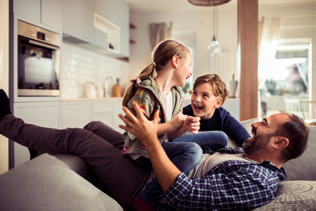 Happy young caucasian family being playful and having fun together on the couch in the living room at home